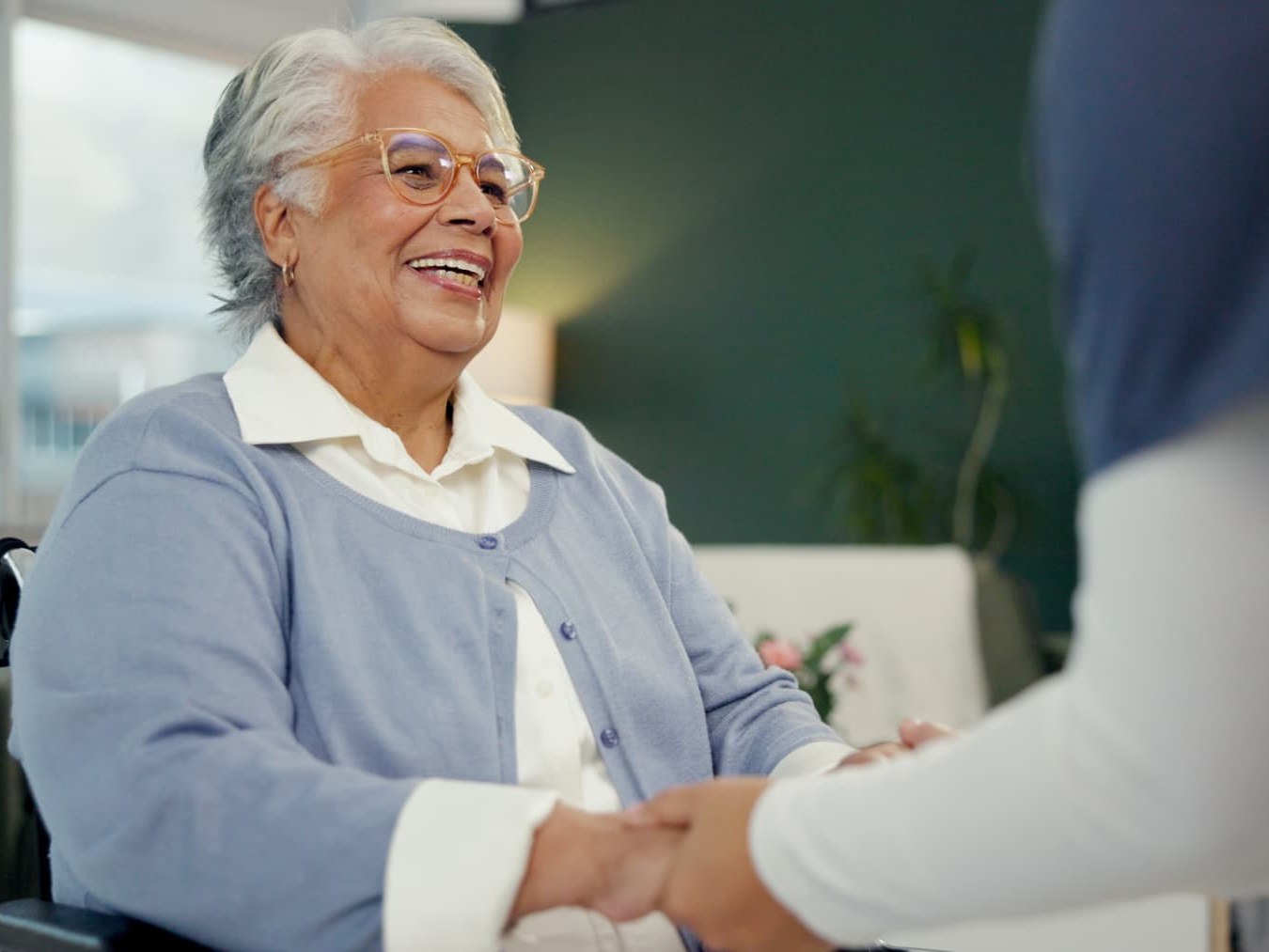 A smiling patient holding hands with her physician during a visit in a post-acute care setting
